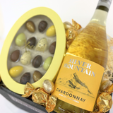 Gavekurv til påske med tropisk Chardonnay, fyldte chokolader, chokoladekugler og dekorativ indpakning klar til påskebordet.